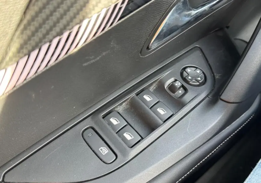 Gros plan sur les commandes des vitres électriques côté gauche d’une Peugeot 2008 Hybrid noire, avec réglage des rétroviseurs.