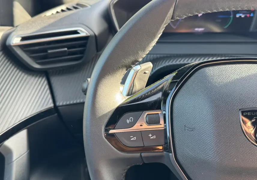 Gros plan sur le volant noir de la Peugeot 2008 Hybrid 136 e-DCS6 Allure avec commandes intégrées et tableau de bord partiel.