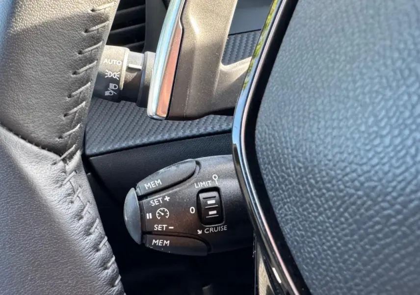 Gros plan sur la commande de régulateur de vitesse au volant cuir noir du Peugeot 2008 Hybrid 136 e-DCS6 Allure.