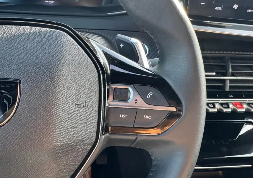 Gros plan sur le volant noir du Peugeot 2008 Hybrid 136 e-DCS6 Allure avec commandes intégrées et partie du tableau de bord.