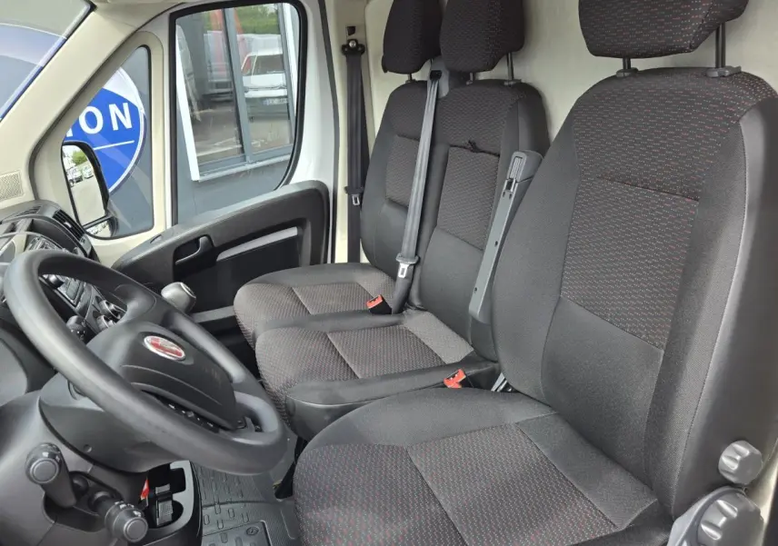 Vue intérieure côté conducteur du Fiat Ducato Fourgon 2023, montrant les sièges noirs avec motifs rouges et le volant.