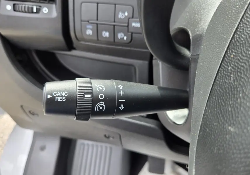 Gros plan sur la commande de régulateur de vitesse à gauche du volant dans l'habitacle noir du Fiat Ducato Fourgon blanc.