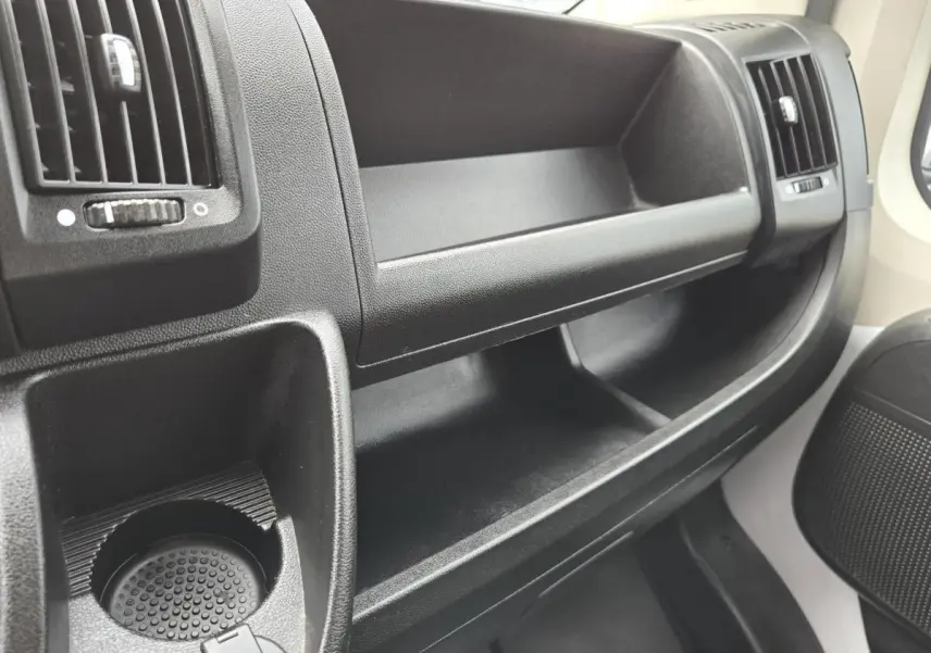 Vue rapprochée de la console centrale noire du Fiat Ducato Fourgon 2023, avec porte-gobelet et aérateurs.