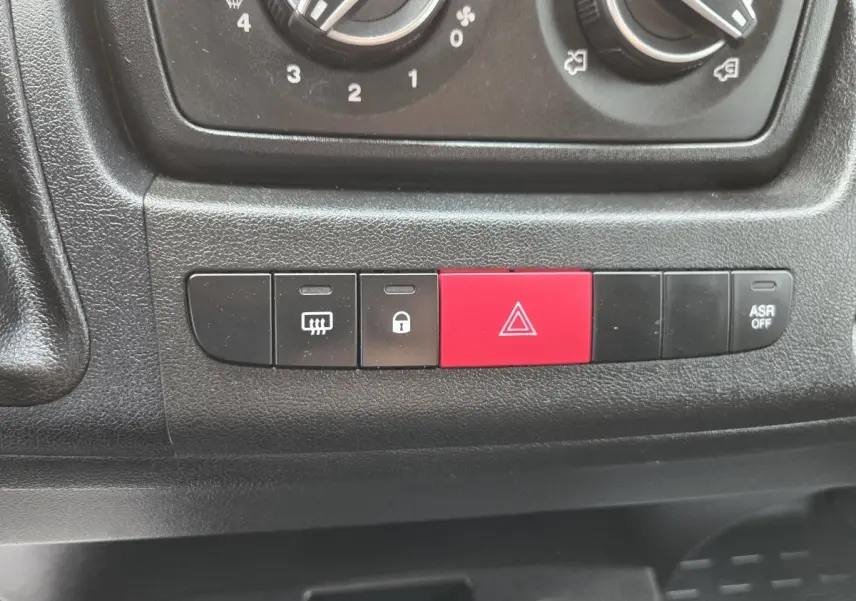 Gros plan sur les boutons de commande du tableau de bord noir du Fiat Ducato Fourgon blanc 2023, avec bouton rouge de warning.