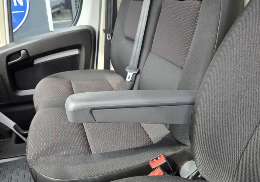 Gros plan sur les sièges avant gris foncé avec motifs rouges du Fiat Ducato Fourgon, côté conducteur, avec accoudoir relevé.