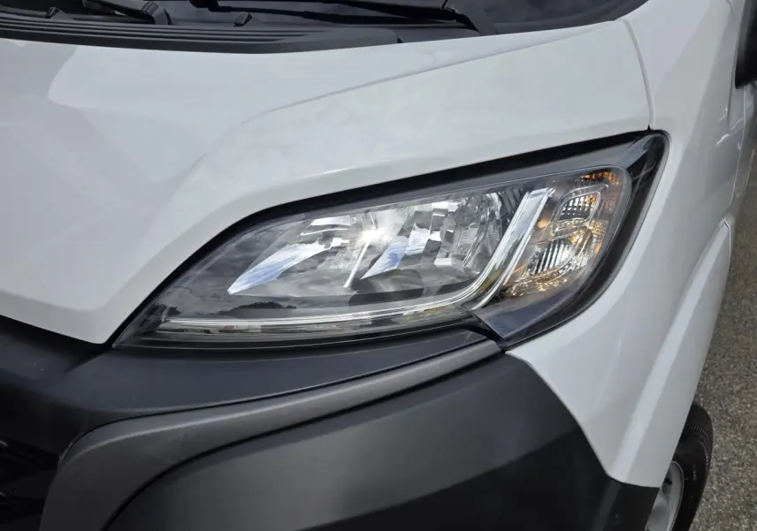 Gros plan sur le phare avant droit d’un FIAT Ducato Fourgon blanc avec pare-chocs noir.