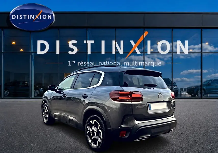Vue 3/4 arrière droite du Citroën C5 Aircross gris platinium avec jantes alu et barres de toit visibles.