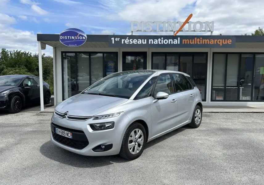 Citroën C4 Picasso gris aluminum vue 3/4 avant droit, stationnée devant un showroom Distinxion.