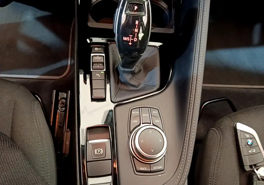 Gros plan sur la console centrale noire du BMW X2 blanc 2023, avec levier de vitesses automatique et molette de contrôle multimédia.