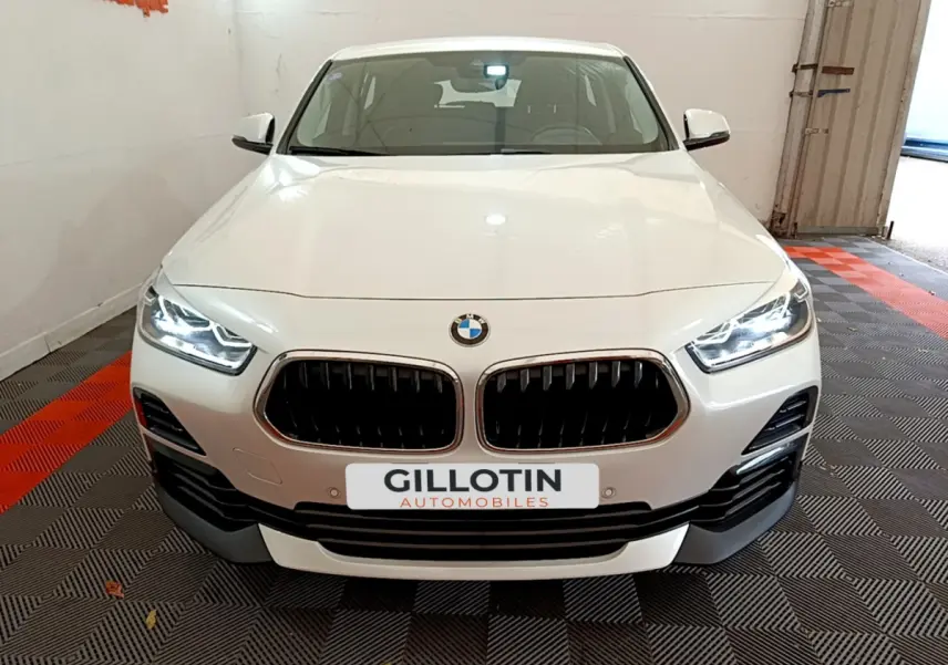 Vue de face d'un BMW X2 blanc avec calandre double haricot et phares LED allumés dans un garage.