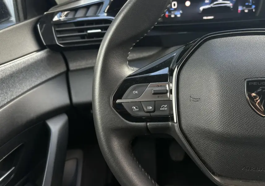 Gros plan sur le volant cuir noir de la Peugeot 308 2024 avec commandes intégrées côté gauche et tableau de bord numérique.
