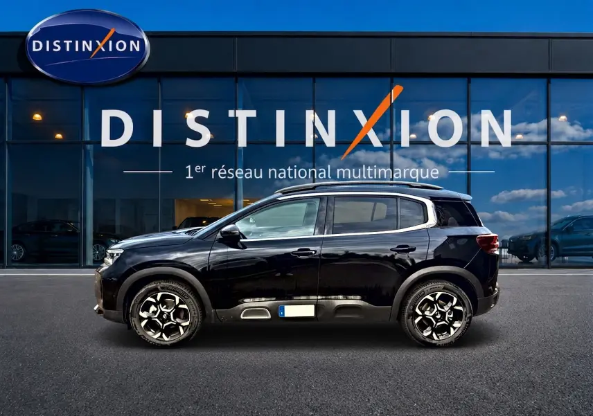 Profil côté gauche d'un Citroën C5 Aircross noir 2025 avec jantes alu et barres de toit devant une vitrine Distinxion.