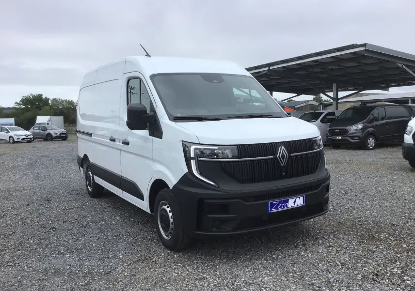 Renault Master blanc en 3/4 avant droit, avec calandre noire et feux LED distinctifs sur un parking gravillonné.