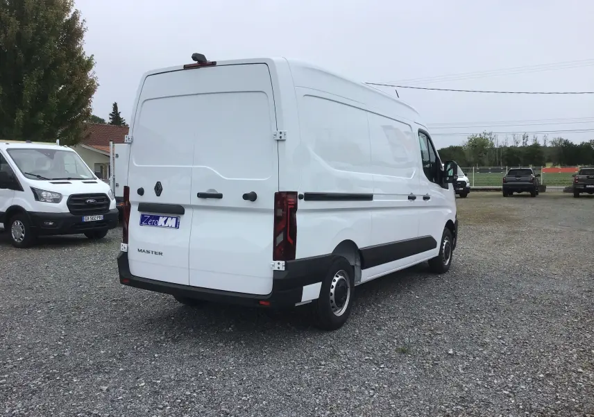 Renault Master blanc en vue 3/4 arrière droit, fourgon utilitaire avec portes arrière fermées sur parking gravel.