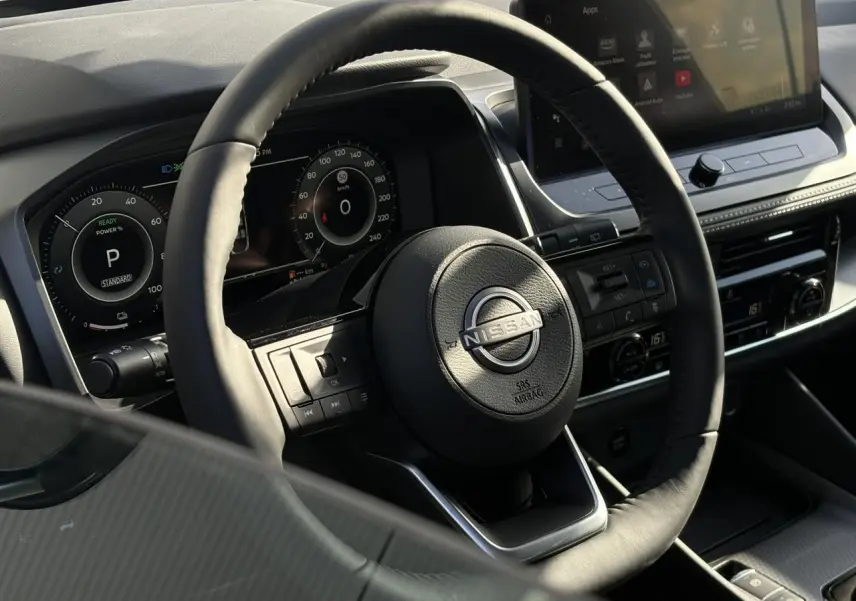 Vue intérieure centrée sur le volant cuir noir et le combiné numérique du Nissan Qashqai 2025, avec écran tactile visible.