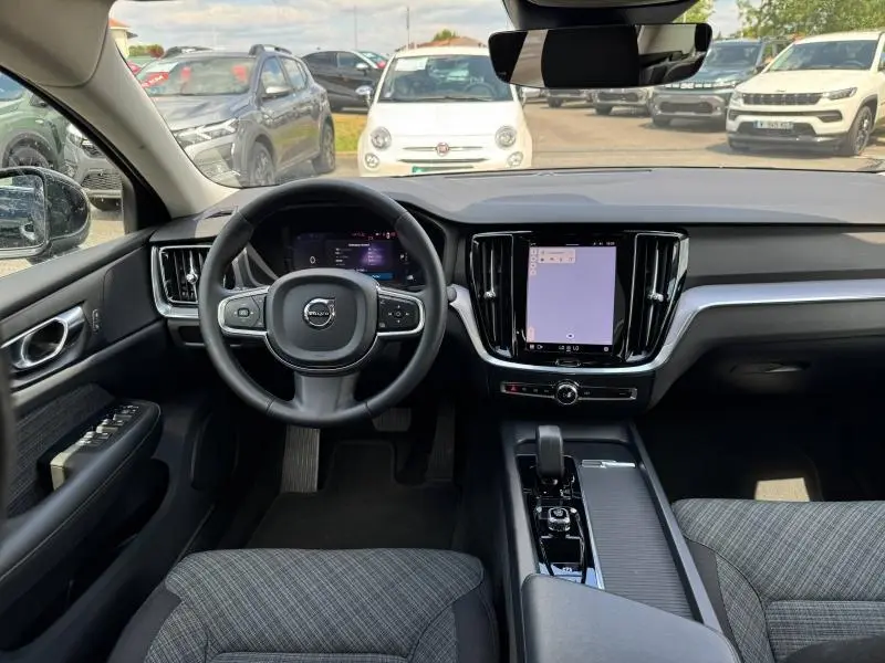 Vue intérieure avant du tableau de bord et volant de la Volvo S60 2024 avec écran tactile vertical et sellerie grise.