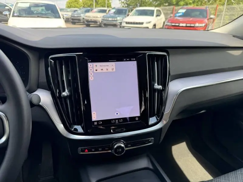 Vue intérieure centrée sur l’écran tactile du tableau de bord du Volvo S60 gris, avec aérateurs noirs brillants.