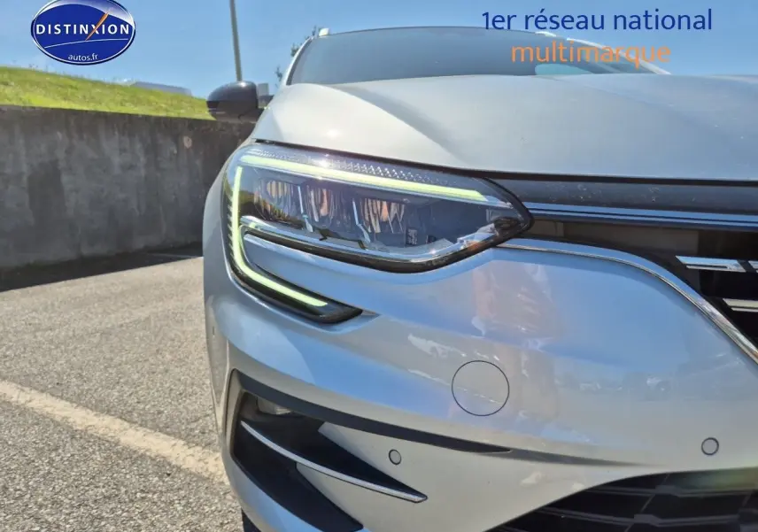Gros plan sur le phare avant gauche d’une Renault Mégane Break gris Titanium avec détails LED et capteurs de stationnement.