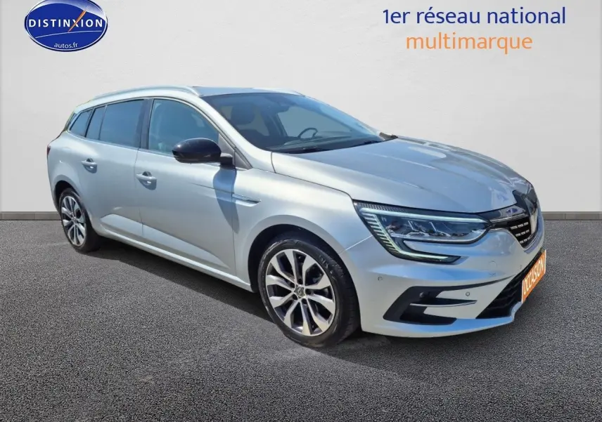 Renault Mégane Break gris titanium vue 3/4 avant droit, avec jantes alliage et barres de toit visibles.