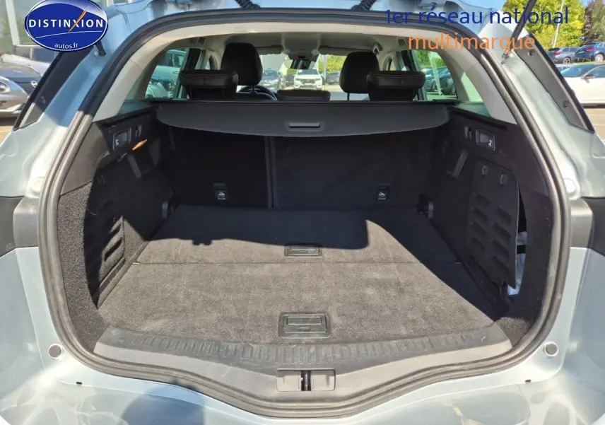 Coffre ouvert vu de l'arrière d'une Renault Mégane Break gris titanium, montrant un espace de chargement spacieux et propre.