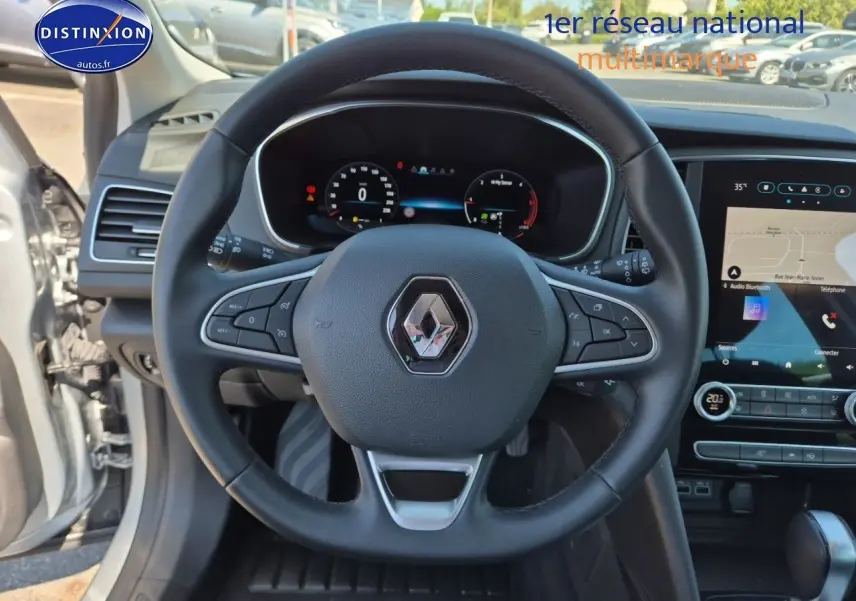 Vue intérieure centrée sur le volant multifonction noir d'une Renault Mégane Break 2024 avec tableau de bord digital et écran tactile.