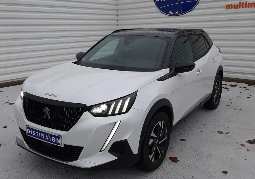 Peugeot 2008 blanc nacré avec toit noir en 3/4 avant droit, phares allumés et attelage visible à l'arrière.
