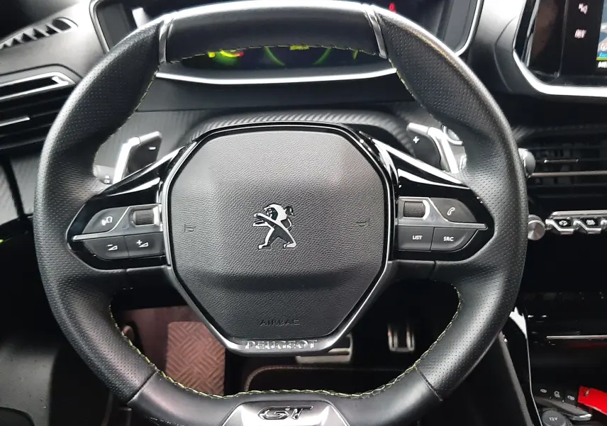 Vue rapprochée du volant cuir GT du Peugeot 2008 2023 avec commandes intégrées et tableau de bord en arrière-plan.