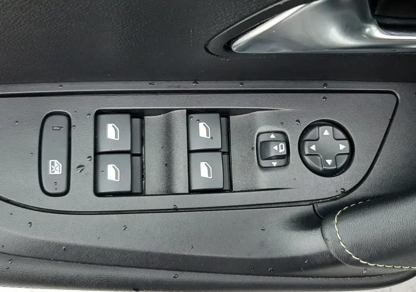 Gros plan sur les commandes des vitres et rétroviseurs côté gauche d'une Peugeot 2008 blanc nacré avec toit noir.