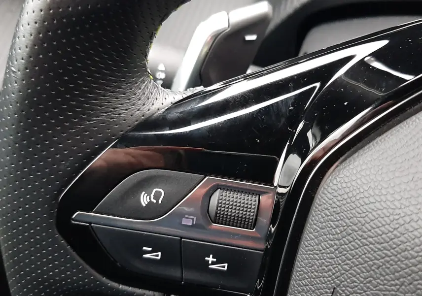 Gros plan sur les commandes gauche du volant en cuir perforé du Peugeot 2008 blanc nacré 2023 avec palettes de changement de vitesse.