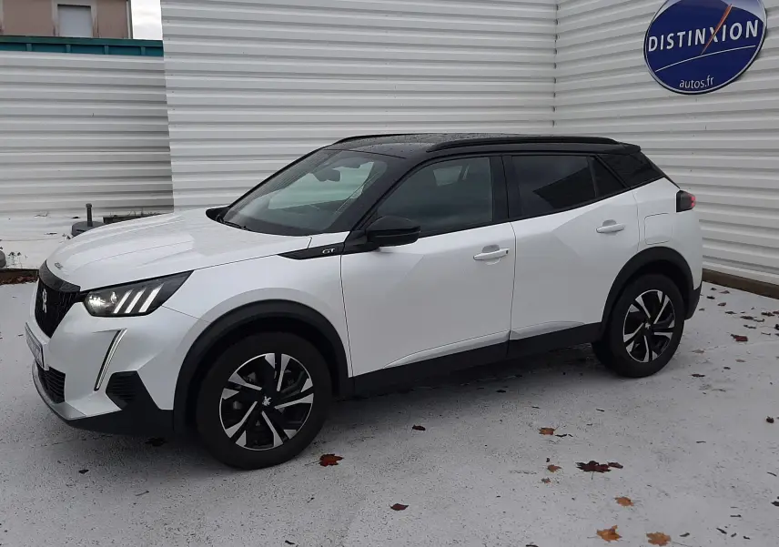 Peugeot 2008 blanc nacré avec toit noir en vue 3/4 avant droit, stationné devant un mur blanc avec logo Distinxion.
