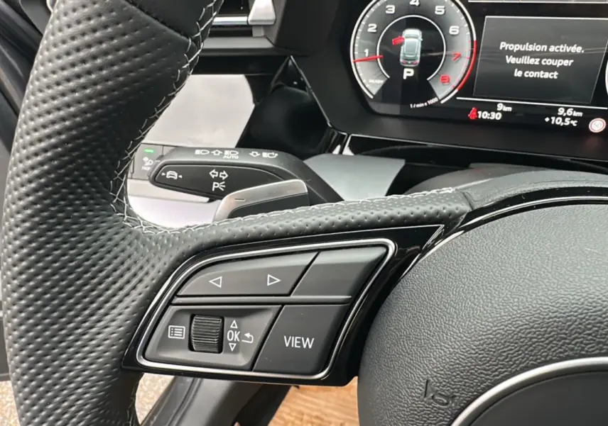 Gros plan sur le volant cuir à méplat et les commandes multifonctions de l'Audi A3 TFSI 150 Hybrid S-Line 2025.