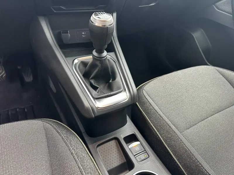 Gros plan intérieur sur la console centrale du Renault Captur 2025 avec levier de vitesse manuel et sièges tissu gris.