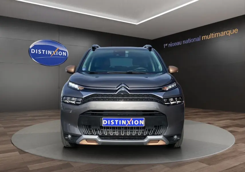 Vue frontale d'un Citroën C3 Aircross gris platinium avec détails bronze sur les rétroviseurs et pare-chocs, en showroom.