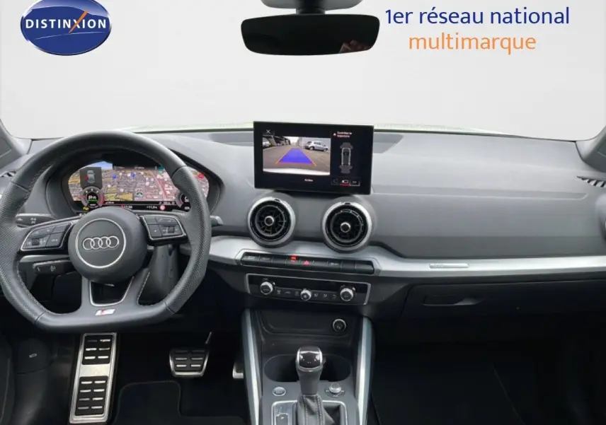 Intérieur Audi Q2 2025 vu de face, tableau de bord noir avec écran central affichant caméra de recul.