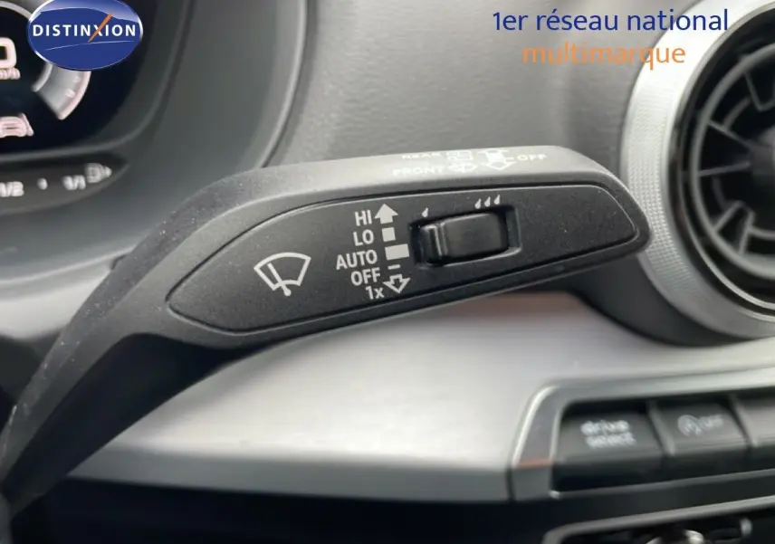Gros plan sur la commande d’essuie-glace à gauche du volant dans l’Audi Q2 argent rose métal, avec tableau de bord partiellement visible.