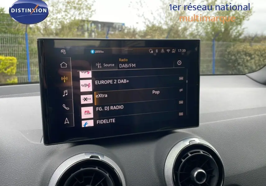 Écran tactile central affichant les stations radio DAB/FM dans l'habitacle d'un Audi Q2 argent rose 2025.