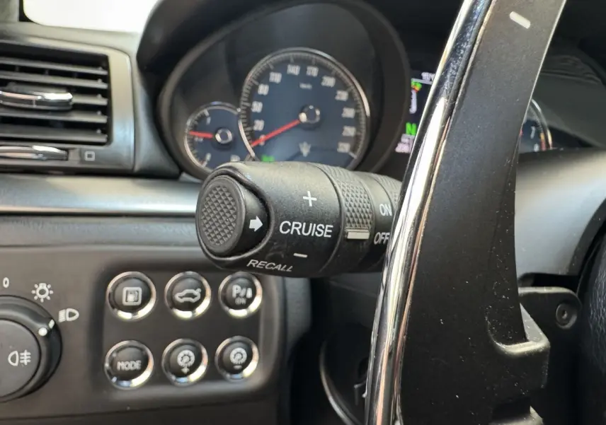 Gros plan sur le volant et commandes du régulateur de vitesse d’une Maserati Granturismo S 4.7 gris foncé, tableau de bord visible.