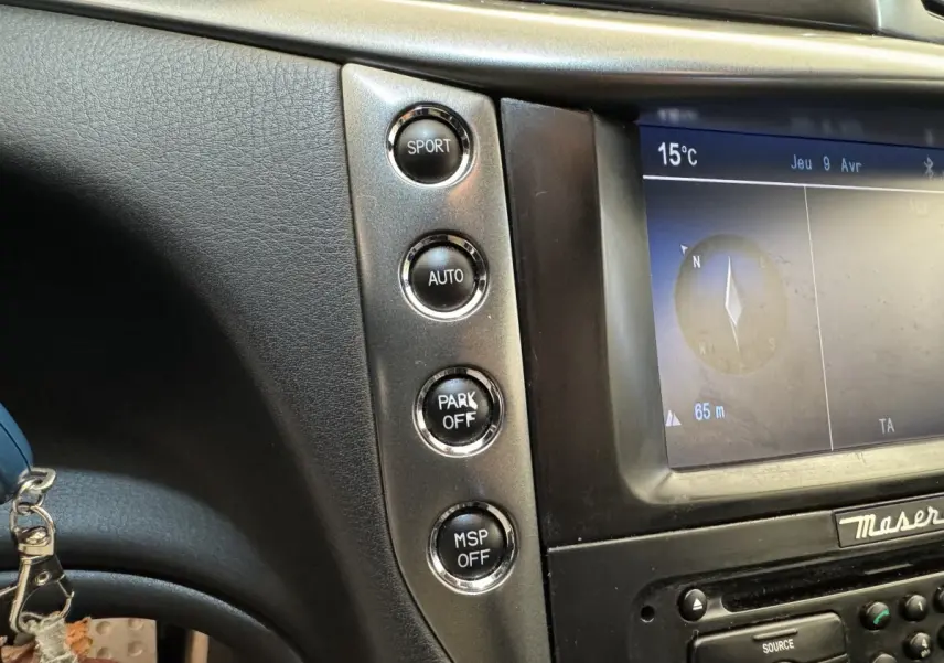 Gros plan sur la console centrale de la Maserati Granturismo S 4.7 2010, boutons de mode sport et écran de navigation visible.