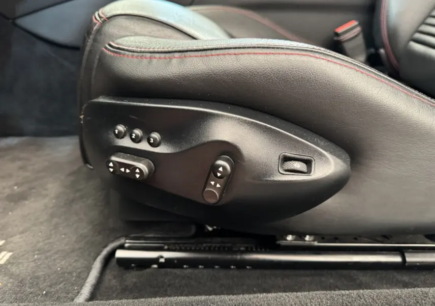 Gros plan sur les commandes électriques du siège conducteur en cuir noir avec surpiqûres rouges d'une Maserati Granturismo S 4.7 gris foncé.