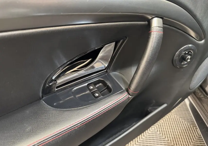 Gros plan sur la poignée et les commandes de fenêtre côté gauche de la porte intérieure noire avec surpiqûres rouges d'une Maserati Granturismo S 4.7.