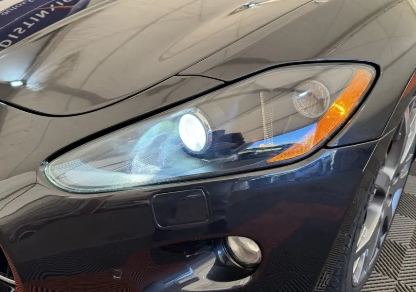 Gros plan sur l'avant droit gris foncé d'une Maserati Granturismo S 4.7 avec phares bi-xénon allumés.