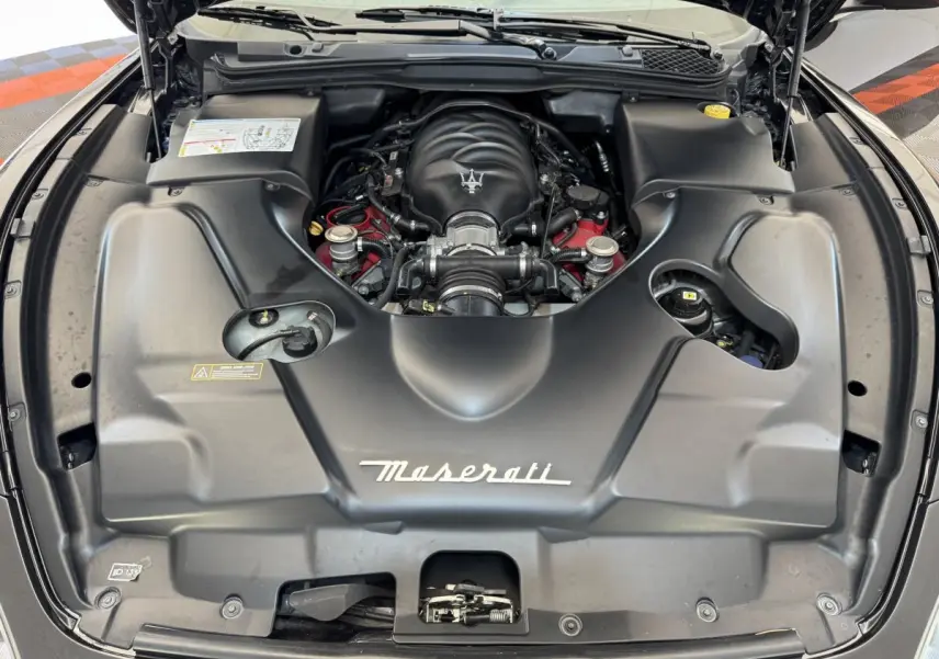 Vue plongeante sur le moteur noir de la Maserati Granturismo S 4.7 gris foncé avec logo Maserati visible.