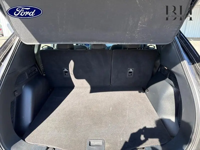 Coffre ouvert vu de l'arrière d'un Ford Kuga noir Agate Métallisée, montrant la banquette arrière rabattue partiellement.