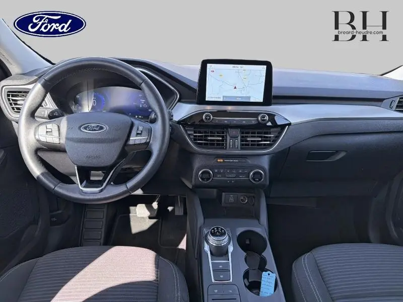 Vue intérieure frontale du tableau de bord et volant cuir multifonction du Ford Kuga 2023 avec écran tactile GPS et console centrale grise.