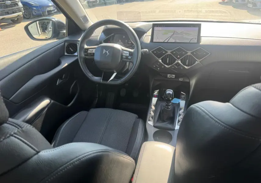 Vue intérieure avant du DS3 2024 gris, montrant le volant, la boîte manuelle et l'écran tactile central avec navigation.