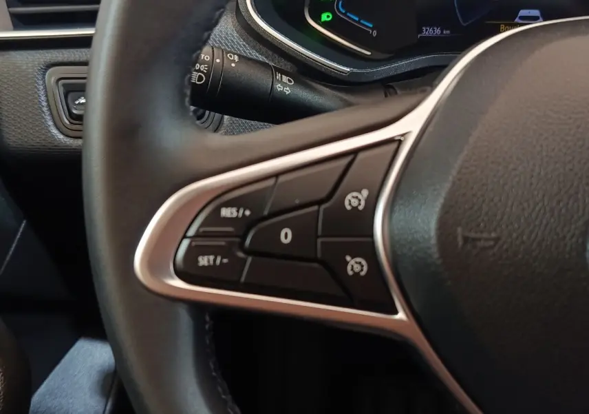 Gros plan sur les commandes du volant cuir synthétique de la Renault Clio Business E-TECH 140 blanc, affichage numérique en arrière-plan.