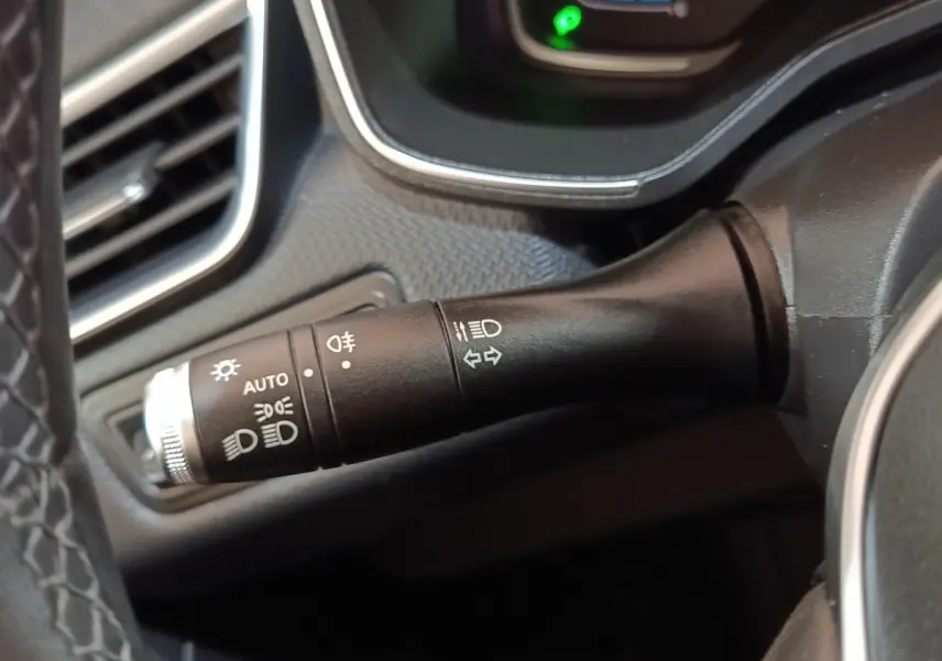 Gros plan sur la commande des phares et clignotants à gauche du volant dans l’habitacle d’une Renault Clio Business E-TECH blanche.