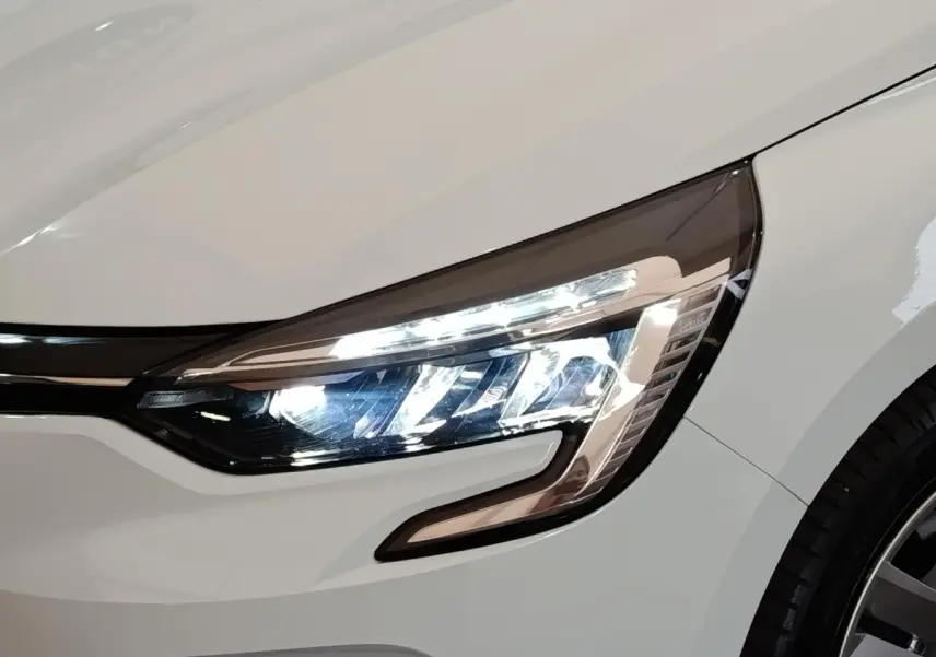 Gros plan sur le phare avant droit allumé d'une Renault Clio Business E-TECH blanche de 2021.