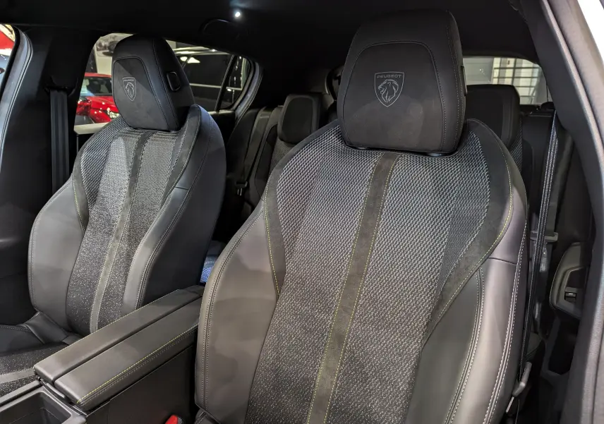 Gros plan sur les sièges avant en cuir noir et tissu gris avec logo Peugeot embossé sur appuie-tête.