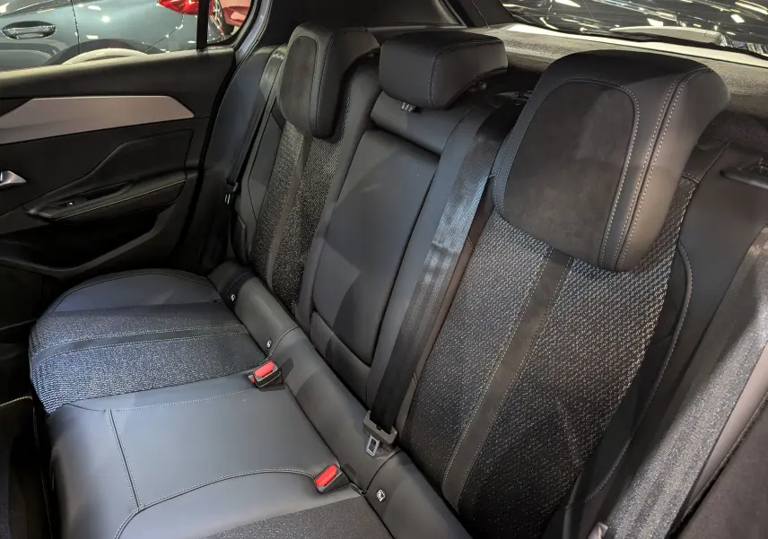 Vue intérieure arrière des sièges en cuir noir et tissu gris de la Peugeot 308 BlueHDi 130 GT 2024, avec ceinture de sécurité visible.